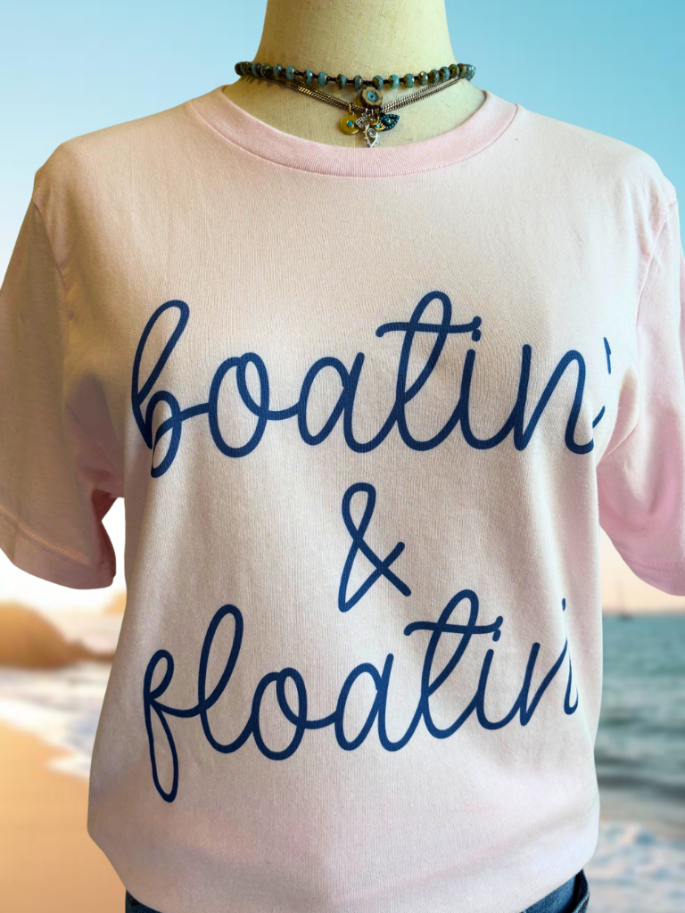 T-shirt with 'boatin' & 'floatin'' text on a beach background. Shown on a form and wearing 2 necklaces