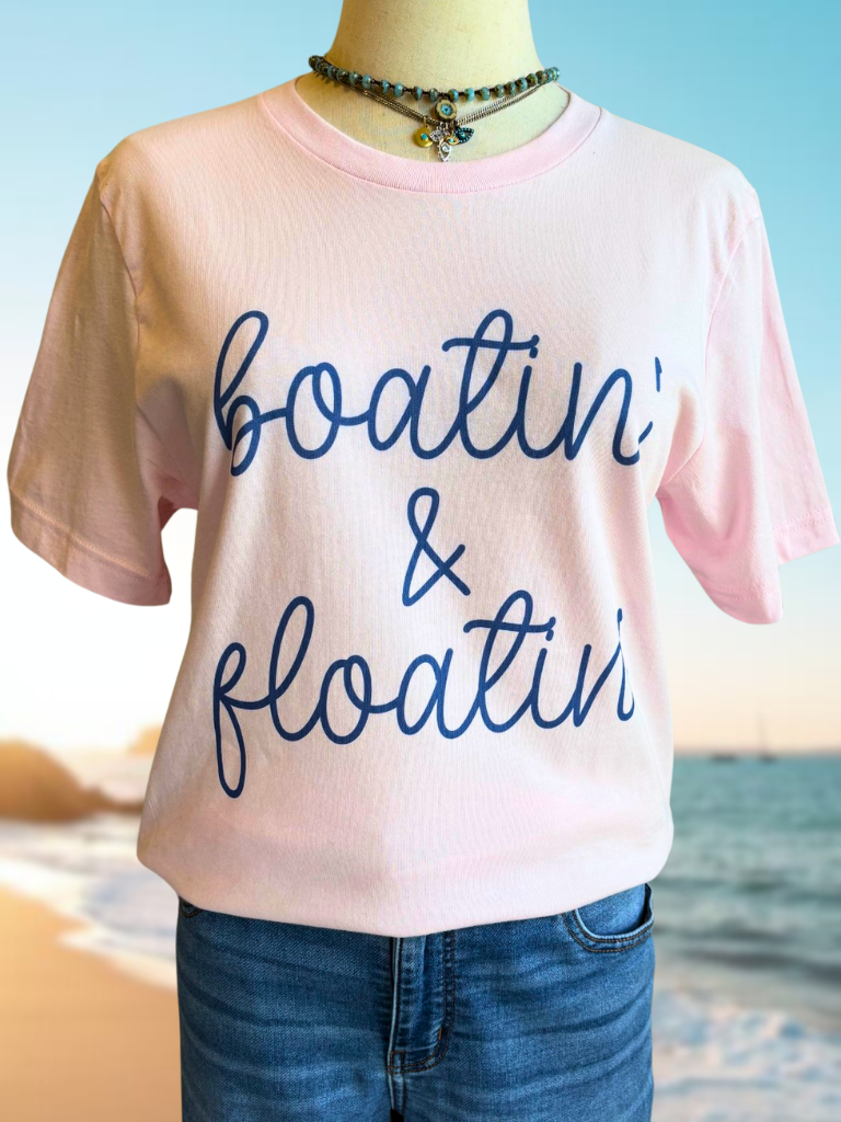 Pink t-shirt with 'Boatin & Floatin' text  in blue, on a beach background, wearing two of our necklaces.