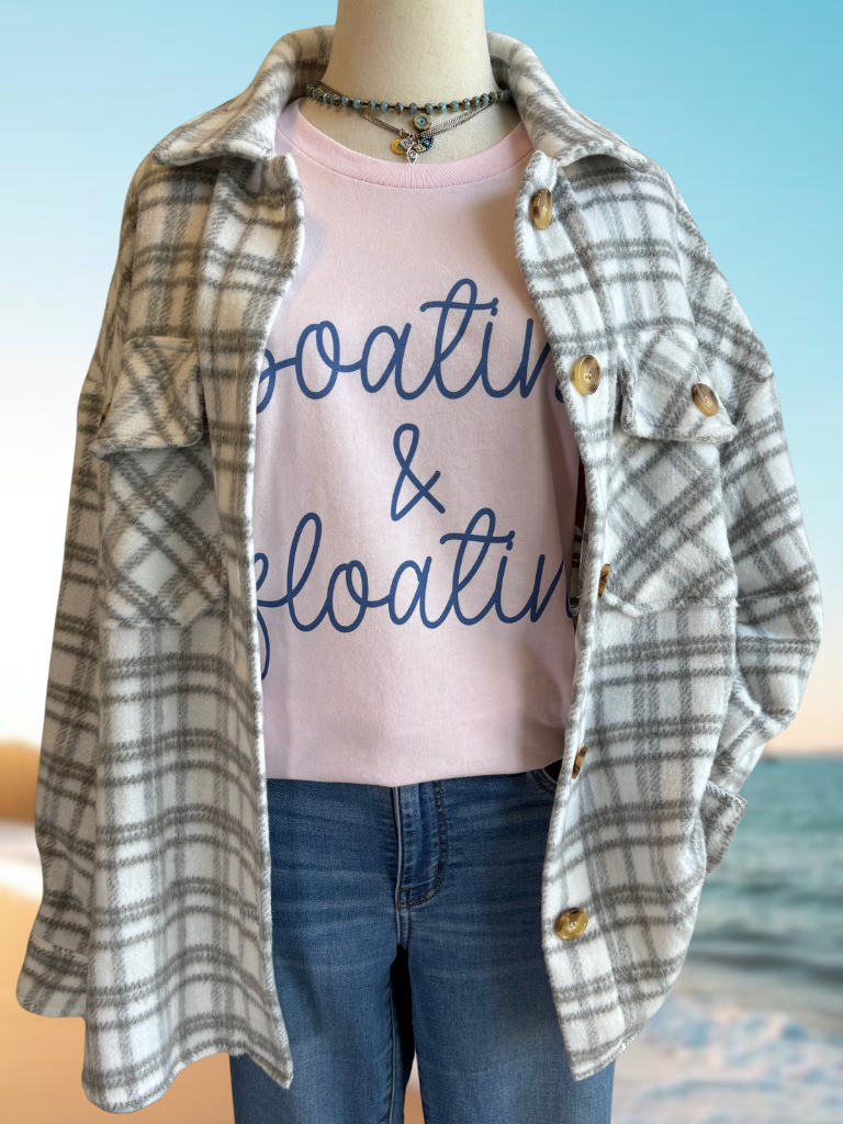 Mannequin wearing our Grey Plaid Shacket over a pink 'Boatin & Floatin' shirt with a beach background, and two necklaces.