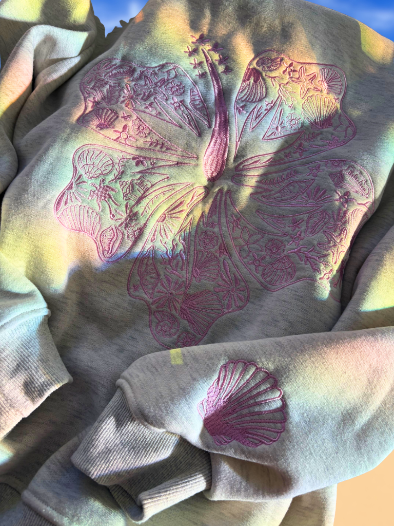 Coastal Bloom Hibiscus Embroidered Zip-Up Ladies Hoodie Front, Flat Lay in the Sun, Shows the  Embroidered Palm Tree on Upper Left Chest and Shell on the Sleeve.