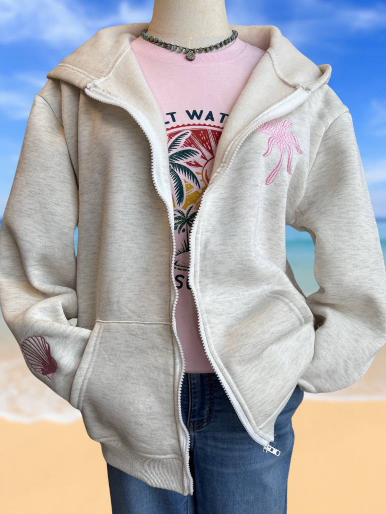 Coastal Bloom Hibiscus Embroidered Zip-Up Ladies Hoodie Front View on Form. Shows the  Embroidered Palm Tree on Upper Left Chest and Shell on the Sleeve. Worn with Our Salty Water Graphic Tee and a Necklace