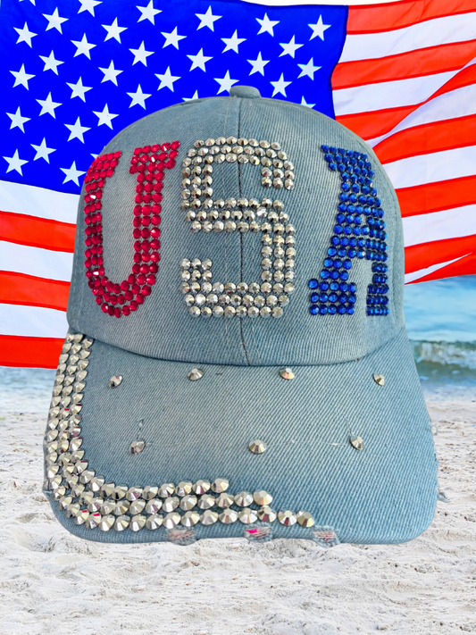 Blue cap with 'USA' in rhinestones against an American flag background