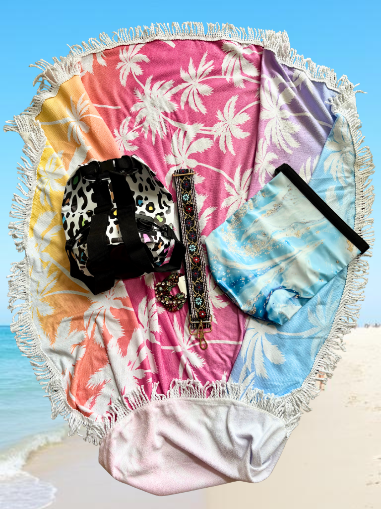 Colorful palm leaf-patterned beach towel with decorative bags on a sandy background