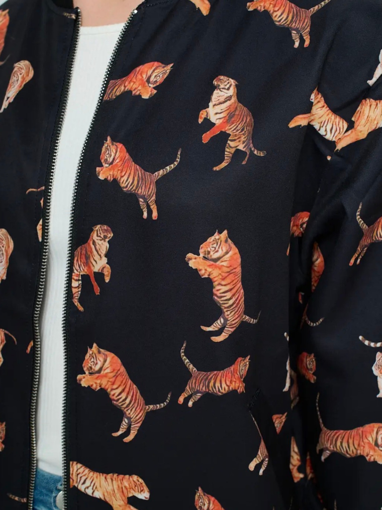 A close-up of a black zip-front jacket featuring an allover print of orange and beige tigers, worn over a white top.